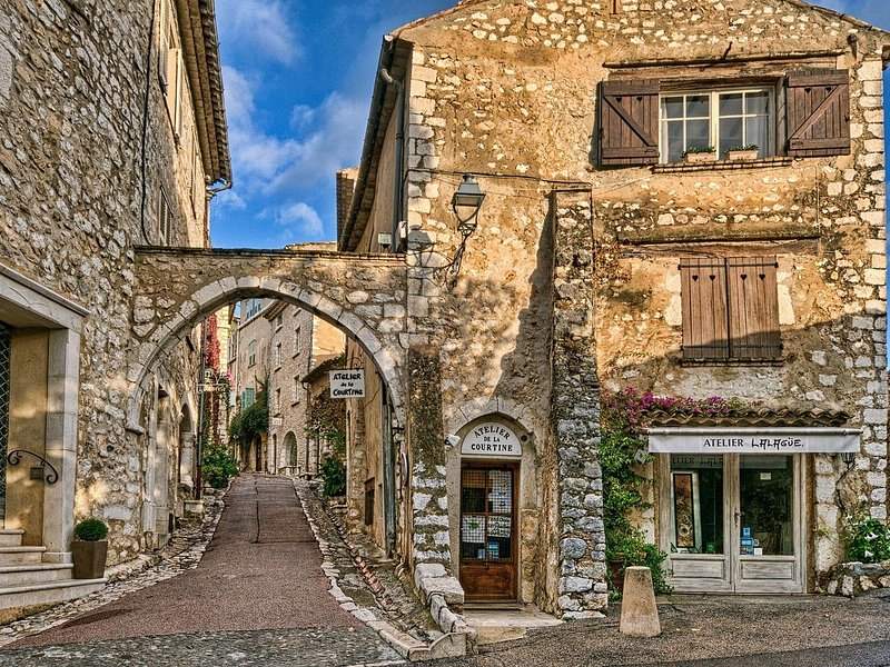 A paved lane, a stone arch and old shopfronts in a hill village