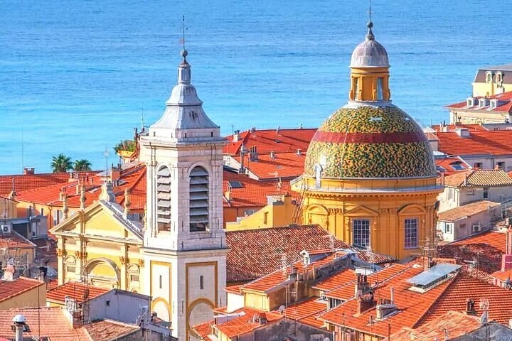 A glazed-tile dome and a white bell tower above red-tiled old town roofs, the sea behind