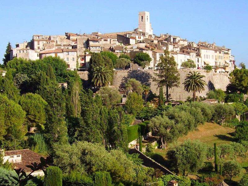 A walled hill village and its church tower on a ridge above cypresses and gardens